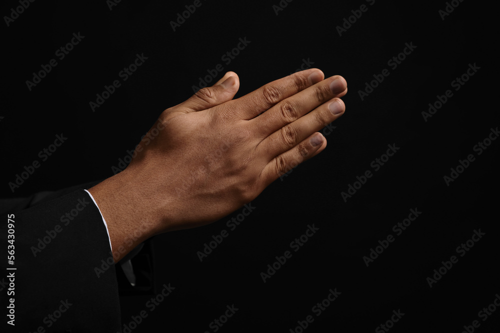 African American man praying to God on black background, closeup of hands