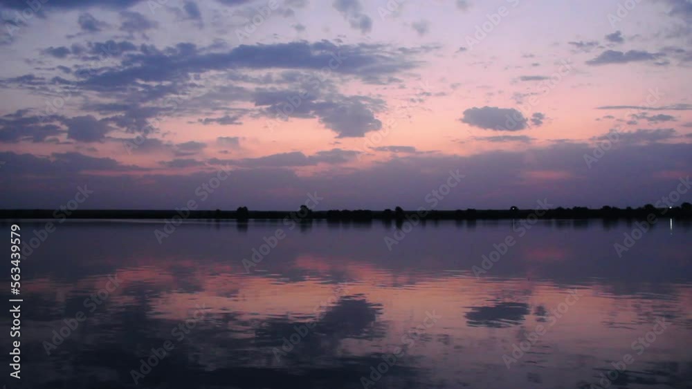 Lake at dawn. Small ripples on the calm water on the background of a forest and a beautiful sunset sky. Beauty wildlife. Natural wallpaper. Blue clouds are reflected in the river. Magnificent nature Lake at dawn. Small ripples on the calm water on the background of a forest and a beautiful sunset sky. Beauty wildlife. Natural wallpaper. Blue clouds are reflected in the river. Magnificent nature