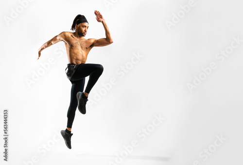 Young athletic Black man doing plyometric lunge jump exercise on white background in an indoor studio