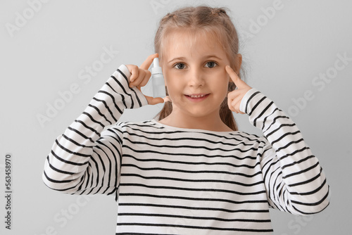 Little girl with eye drops on light background