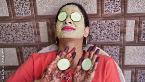 A woman with facial mask and fresh cucumber on eyes relaxing at home. Close-up portrait of smiling girl in clay mask. homemade multani mitti face pack treatment, skin care, beauty.