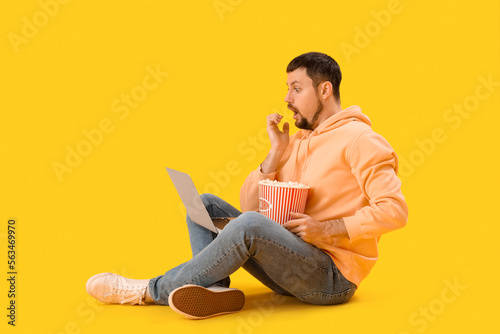 Handsome man with laptop biting nails on yellow background © Pixel-Shot