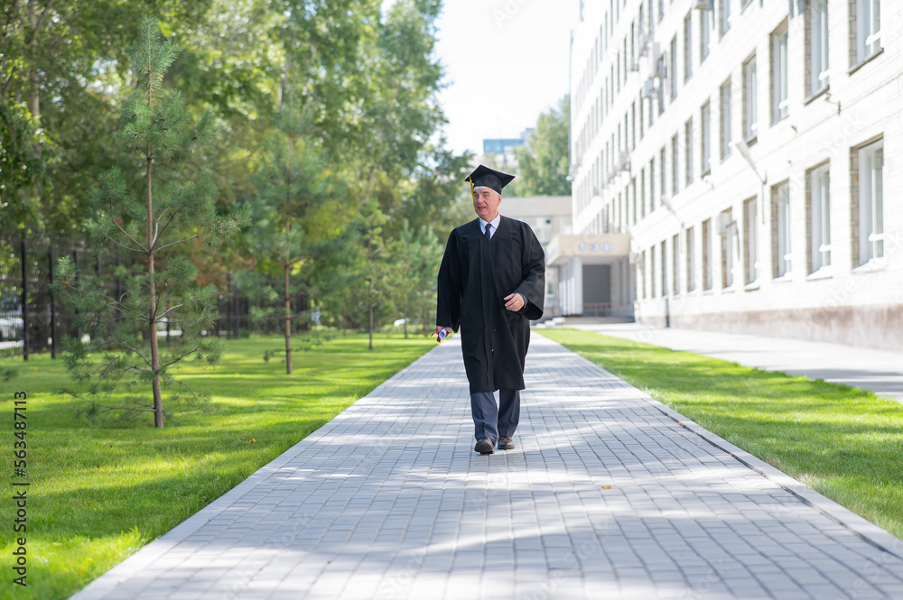 An old man in a graduation gown walks outdoors and holds a diploma. An old man in a graduation gown walks outdoors and holds a diploma.