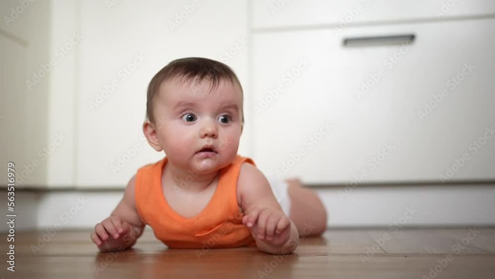 The child lies on the floor in the kitchen looks surprised. family happy childhood. family happy childhood indoors. cute surprised baby lies on the floor lifestyle wants to crawl The child lies on the floor in the kitchen looks surprised. family happy childhood. family happy childhood indoors. cute surprised baby lies on the floor lifestyle wants to crawl