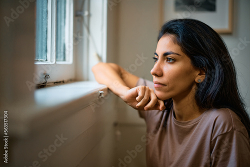 Pensive woman looking through window at home.