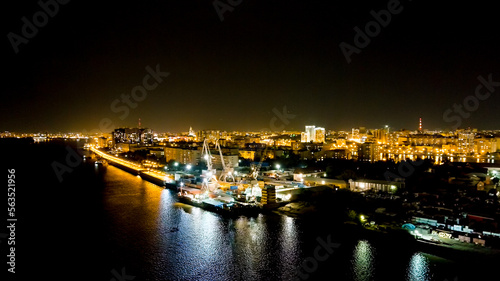 Astrakhan, Russia. Port cranes unload dry cargo. Working port. Embankment of the Volga River. Night city lights, Aerial View