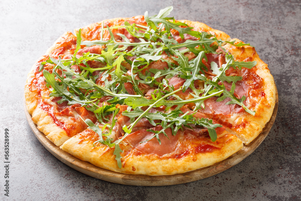 Hot pizza with prosciutto and arugula close-up on a wooden board on the table. Horizontal