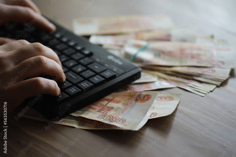 Stacks of 5000 ruble banknotes on the table next to the laptop. Savings and investments in the conditions of sanctions and inflation. Stacks of 5000 ruble banknotes on the table next to the laptop. Savings and investments in the conditions of sanctions and inflation.