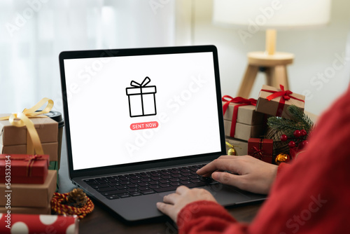 Hand using laptop with sent gift to online application and festive decorations on the black background.