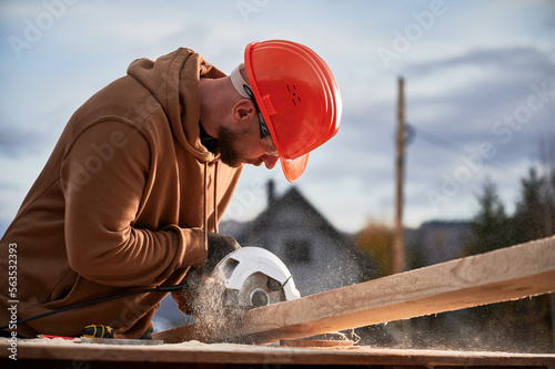 Carpenter using circular saw for cutting wooden plank. Man worker building wooden frame house. Carpentry concept.