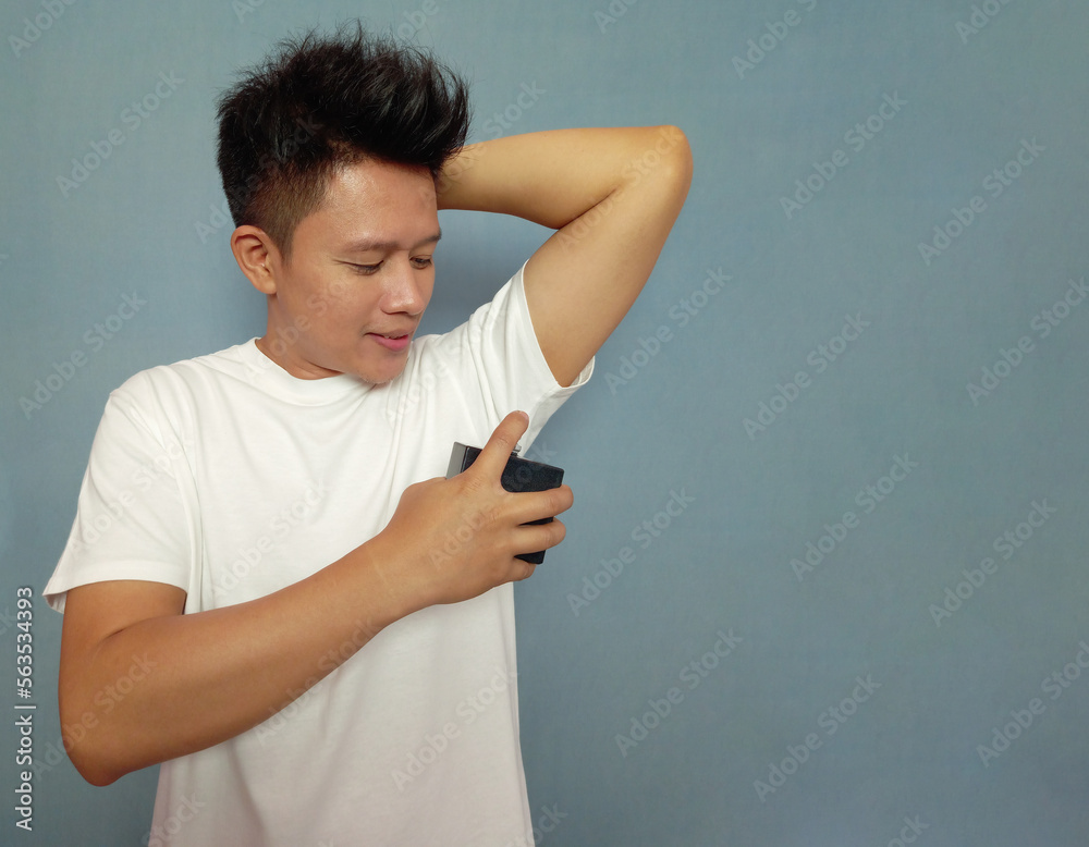 Man wearing white shirt spraying perfume into his armpits Stock Photo