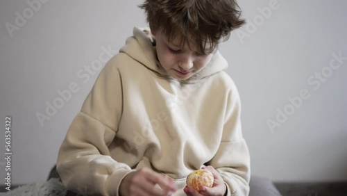 Calm Caucasian teenager peeling tangerine. Boy slowly peels the fruit and breaks it into pieces. photo