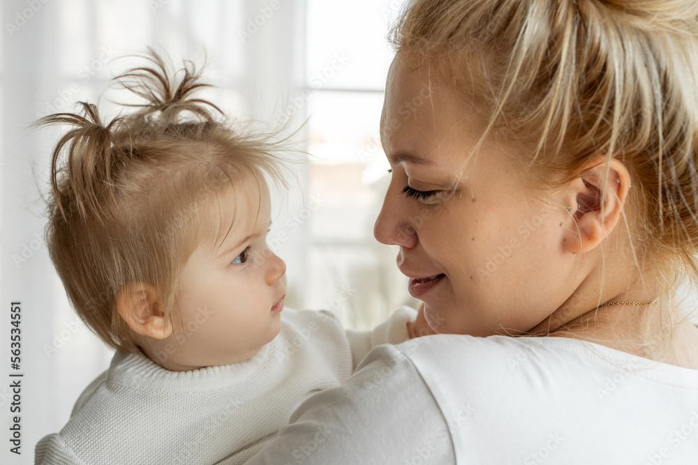 Mom Embrace Her Baby Toddler Girl Near Window At Home. Feeling Happiness, Adopt Family, Love And Care, Parenthood And Childhood. Mom Embrace Her Baby Toddler Girl Near Window At Home. Feeling Happiness, Adopt Family, Love And Care, Parenthood And Childhood.