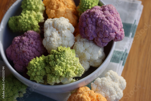 Various sort of cauliflower in a bowl on wooden table. Purple, yellow, white and green color cabbages and green Romanesco or Roman cabbage