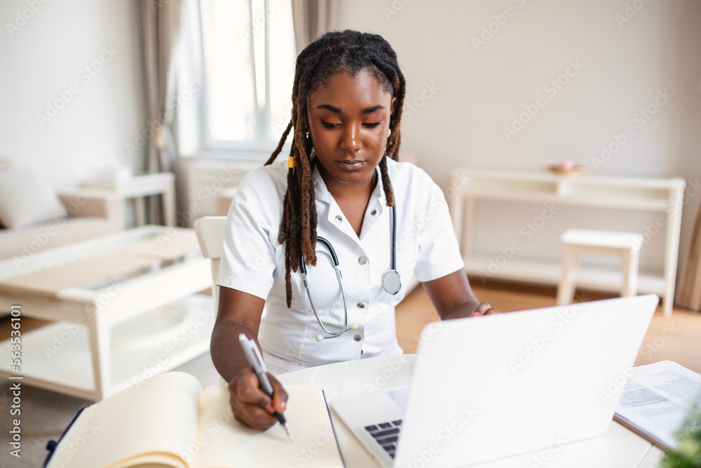 African professional female doctor wearing uniform taking notes in medical journal, filling documents, patient illness history, looking at laptop screen, student watching webinar African professional female doctor wearing uniform taking notes in medical journal, filling documents, patient illness history, looking at laptop screen, student watching webinar