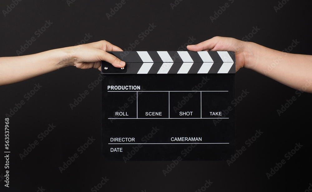 Two hands send and hold Black clapper board or movie slate on black background..