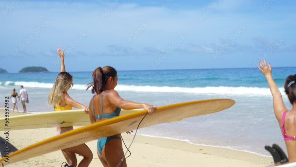 4K Group of Asian woman surfer in swimwear holding surfboard walking to the ocean on tropical beach in sunny day. Girl friends enjoy outdoor activity lifestyle water sport surfing on summer vacation.