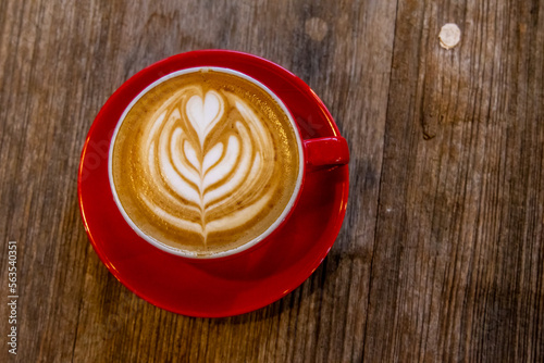 A red cup of coffee cappuccino with latte art on wooden background. Coffee house