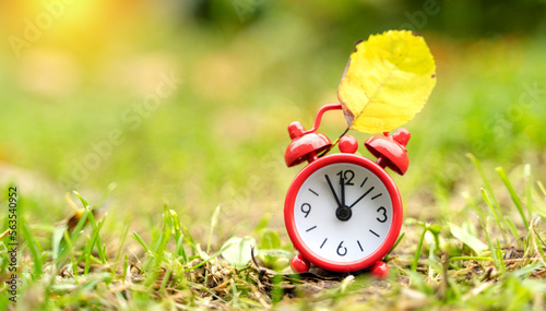 red alarm clock and yellow leaf on the grass, the concept of the end of summer
