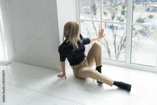 Side view of young businesswoman in white shirt sitting on floor near window