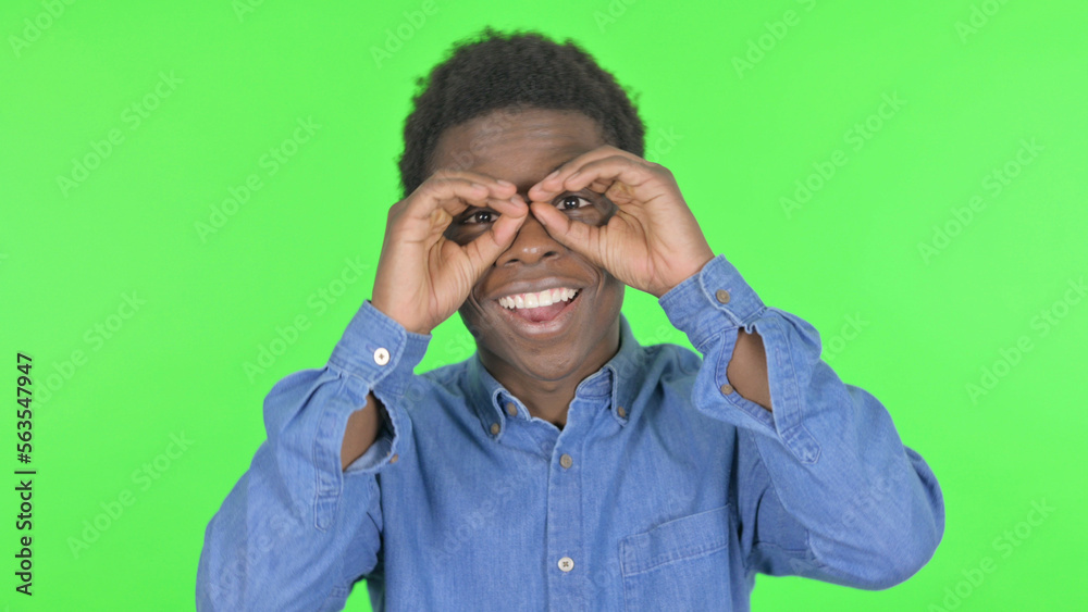 Young African Man Looking Around with Handmade Binocular on Green Background Young African Man Looking Around with Handmade Binocular on Green Background
