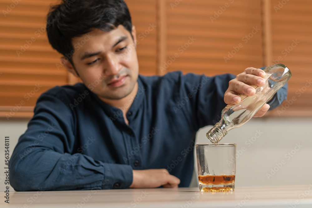 Alcoholism, depressed asian young man pouring, holding bottle whiskey into the glass, drinking alcohol beverage at night. Treatment of alcoholic addiction, suffer abuse problem alcoholism concept. Alcoholism, depressed asian young man pouring, holding bottle whiskey into the glass, drinking alcohol beverage at night. Treatment of alcoholic addiction, suffer abuse problem alcoholism concept.