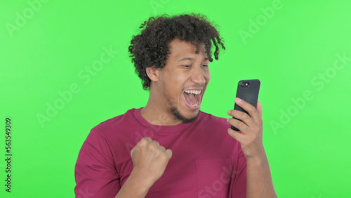 African Man Celebrating on Smartphone on Green Background