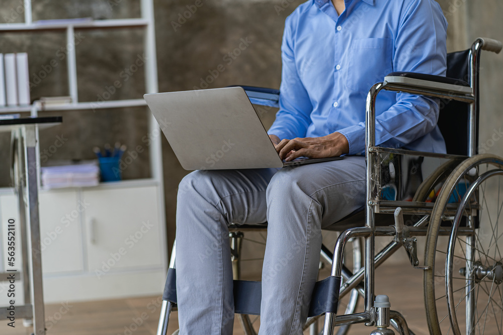 Asian male businessman sitting in wheelchair typing laptop at work