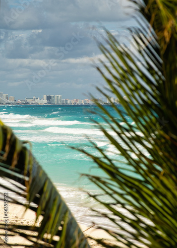 Traumhafter Blick durch Palmenwedel auf das türkise Meer in Mexiko - im Hintergrund die Skyline von Cancun