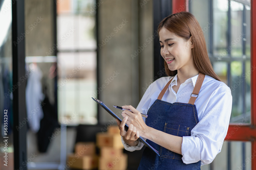 Happy Asian young woman business owner preparing parcel boxes and checking orders for delivery to customer on laptop computer at home, SME marketing, online shopping concept. Happy Asian young woman business owner preparing parcel boxes and checking orders for delivery to customer on laptop computer at home, SME marketing, online shopping concept.