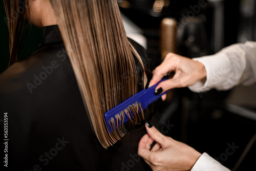Professional hairdresser is combing the wet hair of the female client. Close-up