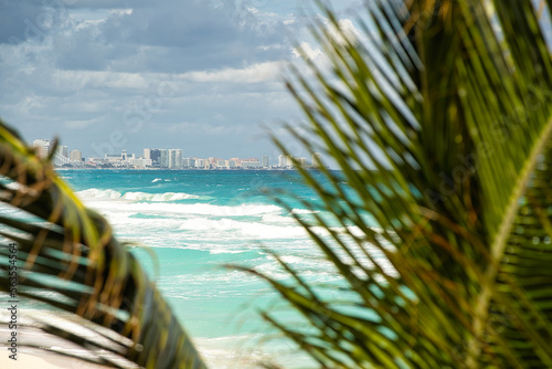 Traumhafter Blick durch Palmenwedel auf das türkise Meer in Mexiko - im Hintergrund die Skyline von Cancun photo