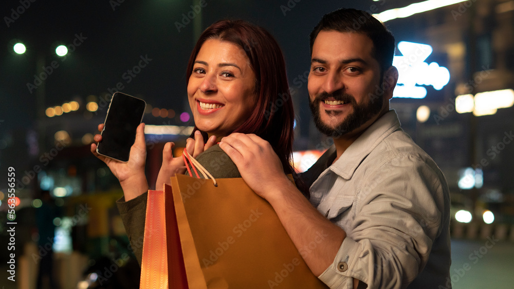 couple shopping at night and showing blank screen of smartphone