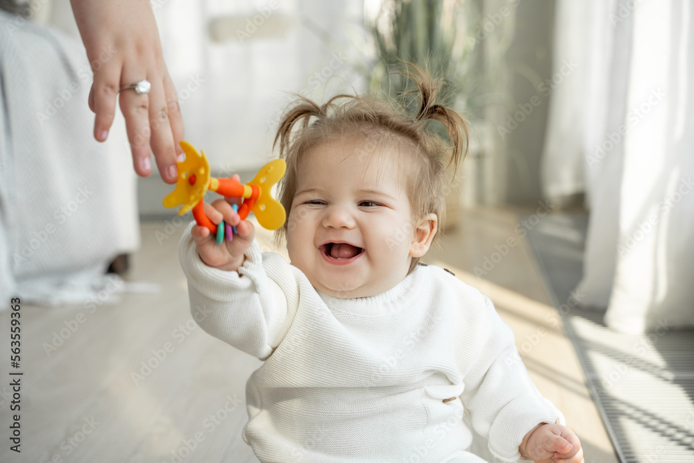 Mom giving to smiling baby favorite toy rattle teether. Child toothache teething, dentition, growing teeth. Care of children, colorful game, Parent care of kids.