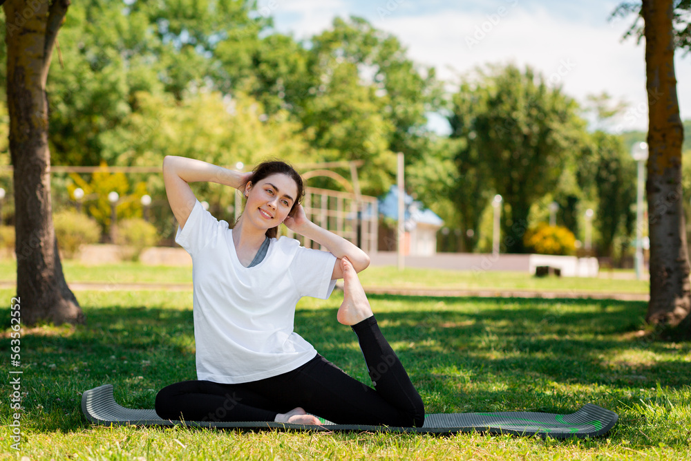 Yoga. A young pretty woman in sportswear performs an exercise sitting on a Mat in a Park on the grass. The concept of a healthy lifestyle