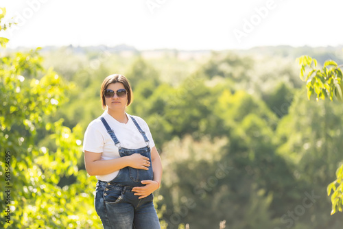 Portrait of a happy and proud pregnant woman looking at her belly in a park at sunrise with a warm back light in the background