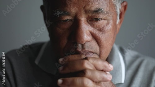 Lonely elderly Asian man sitting alone bowed his head praying to God on a gray background at home. Holding hands in prayer, Close up