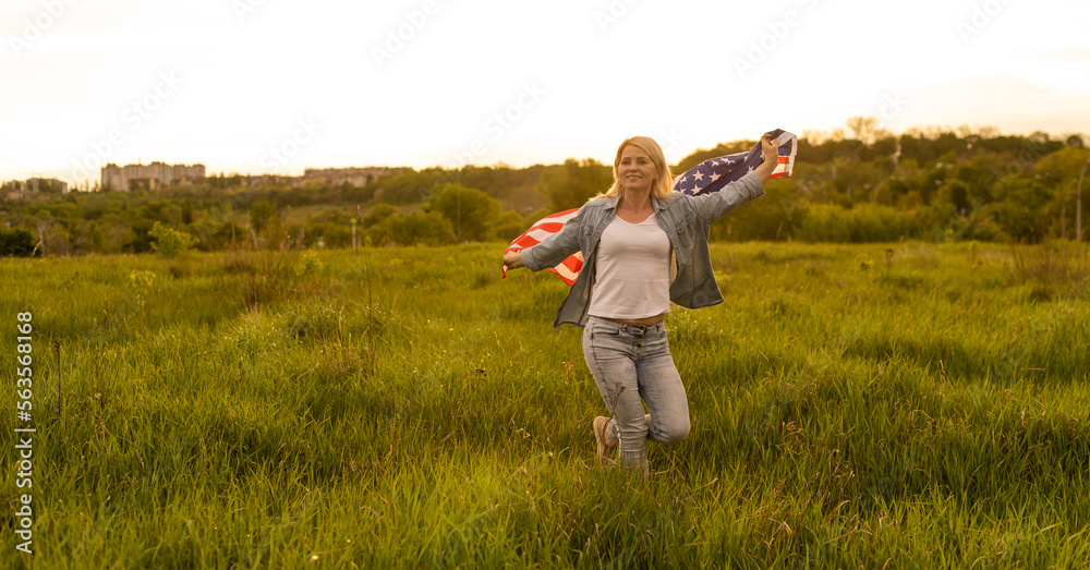 attractive woman holding an American flag in the wind in a field. Summer landscape against the blue sky. Horizontal orientation. attractive woman holding an American flag in the wind in a field. Summer landscape against the blue sky. Horizontal orientation.