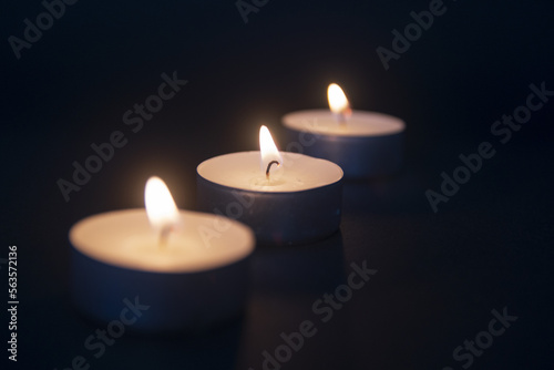 3 tea light candles burning on black background