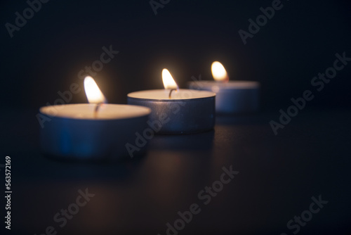 3 tea light candles burning on black background