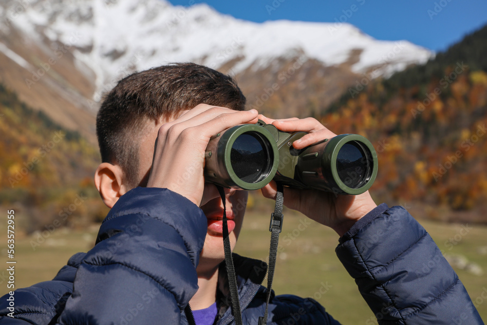 Boy looking through binoculars in mountains on sunny day