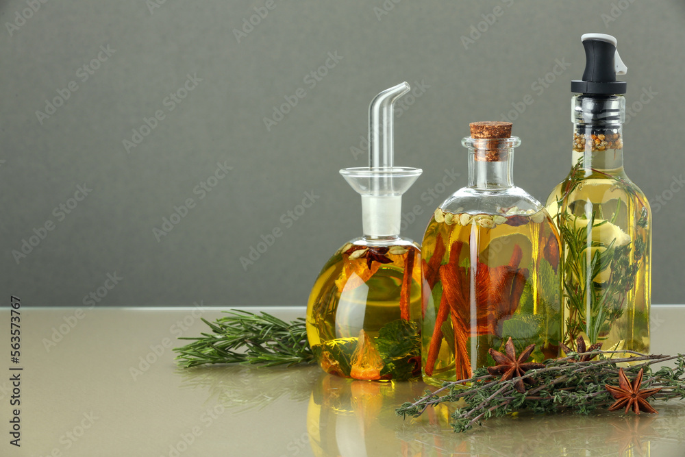 Cooking oil with different spices and herbs in bottles on beige table. Space for text
