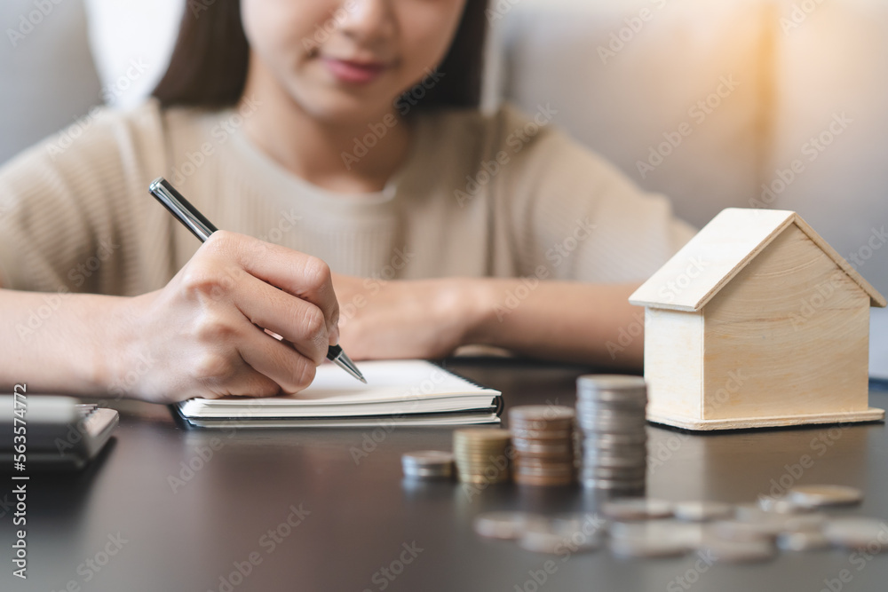 Fototapeta premium Close up hands of Woman putting coin into piggy bank house model saving for buy property