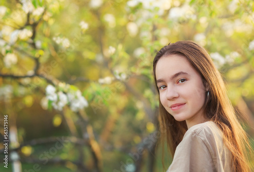 Beautiful teenager girl with blooming apple flowers. Happy cute kid having fun outdoors at sunset.