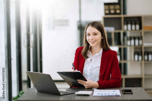 Young beautiful woman typing on tablet and laptop while sitting at the working wooden table modern office.