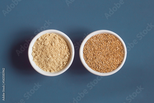 Top view of a close-up of two ceramic bowls side by side with whole and powdered flax seeds. Superfood.