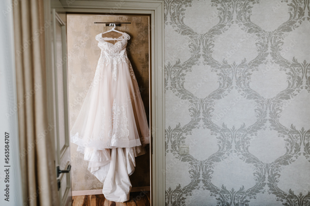 Wedding dress hanging against a wall background in the room. Wedding dress hanging against a wall background in the room.