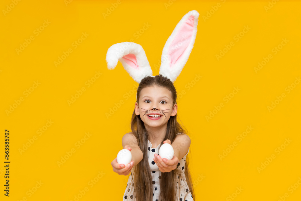 A little joyful girl holds chicken Easter eggs in her hands and smiles, beautiful rabbit ears on the little girl's head.