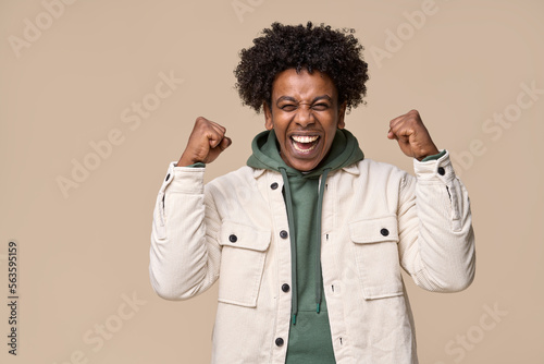 Obraz na płótnie Happy excited lucky African teen winner student boy feeling joy, screaming, celebrating great result or achievement win with victory emotion yes gesture isolated on beige background