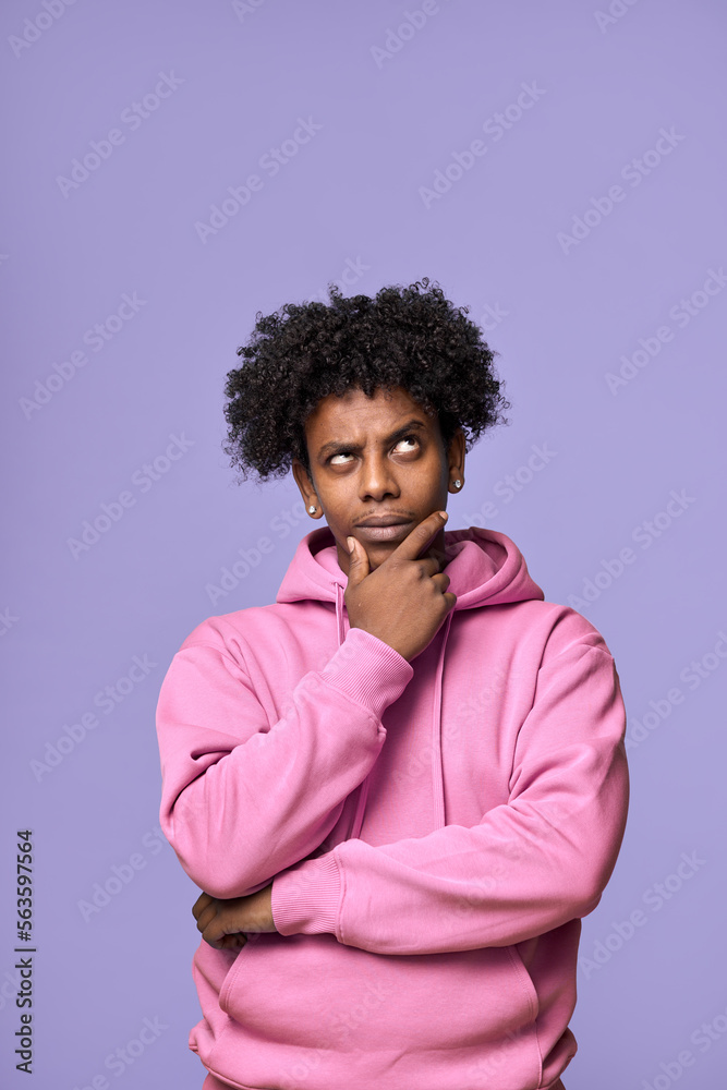 Young thoughtful confused African American teen guy student thinking holding hand on chin, looking up, choosing, making decision, feeling doubt, having question isolated on purple background. Young thoughtful confused African American teen guy student thinking holding hand on chin, looking up, choosing, making decision, feeling doubt, having question isolated on purple background.